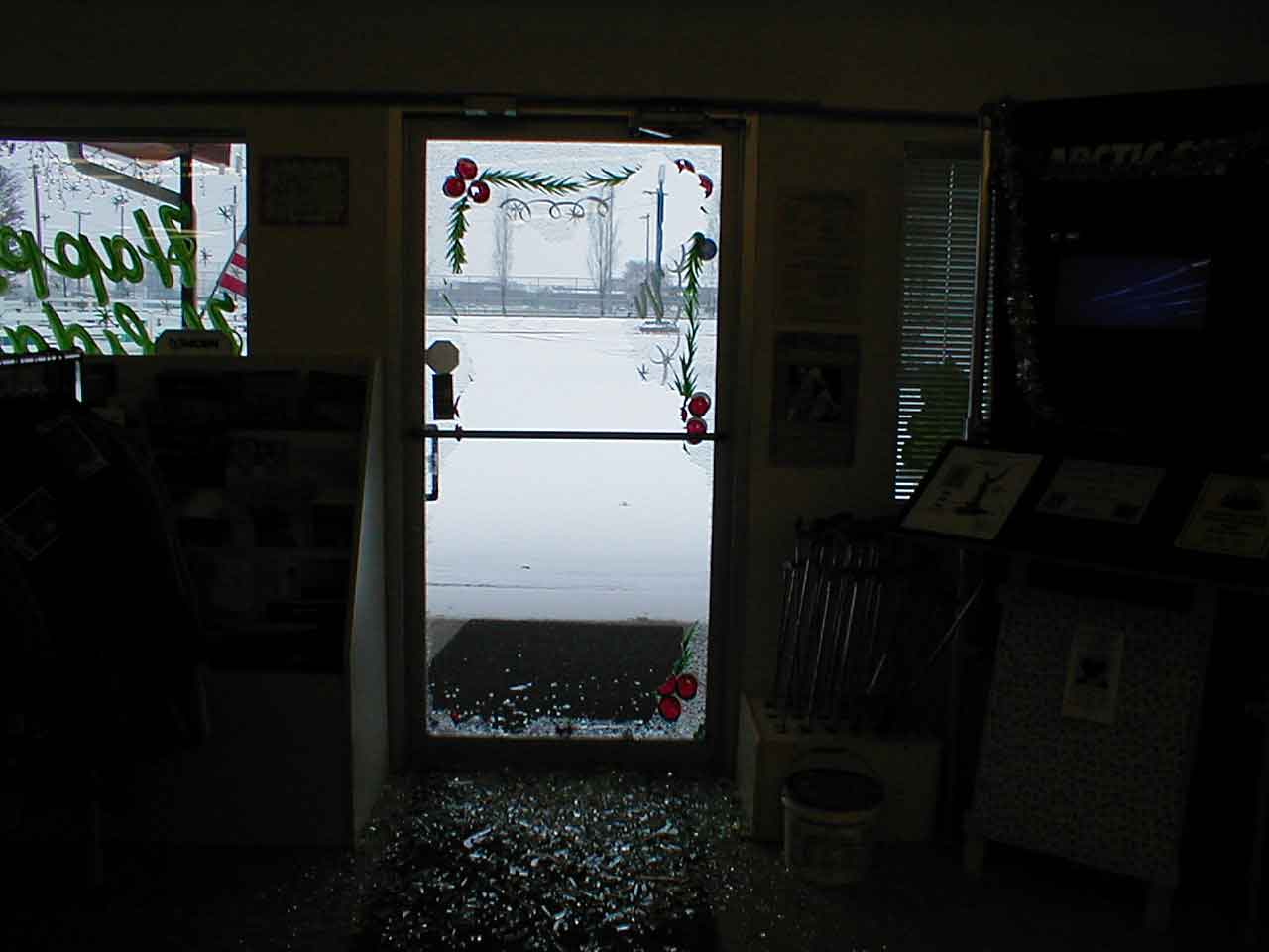 Interior shot of the broken door and broken glass on the floor. You can see Christmas decorations on the outside of the door.