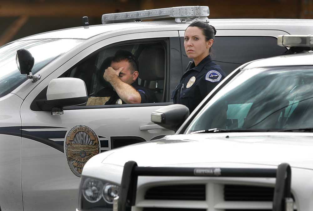A police officer is in the driver seat of a police SUV with his head in his hands, A female officer stands next to the vehicle looking into the distance