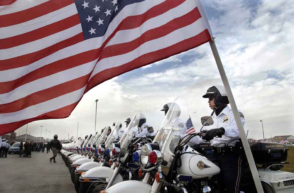 An American flag flies in front of a row of motorcyce officers