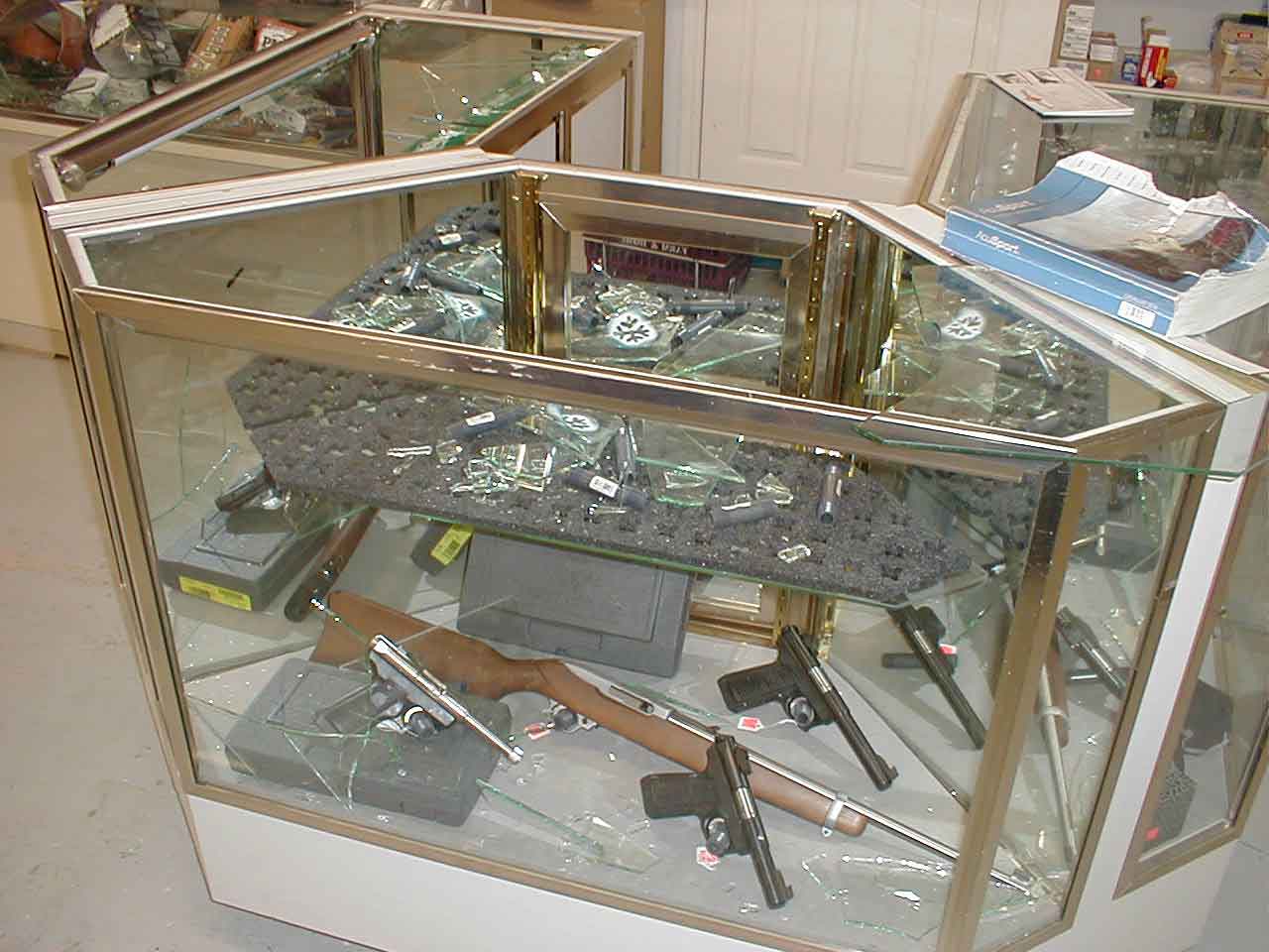 A gun case that has been broken into. Glass is everywhere and there are firearms left behind.