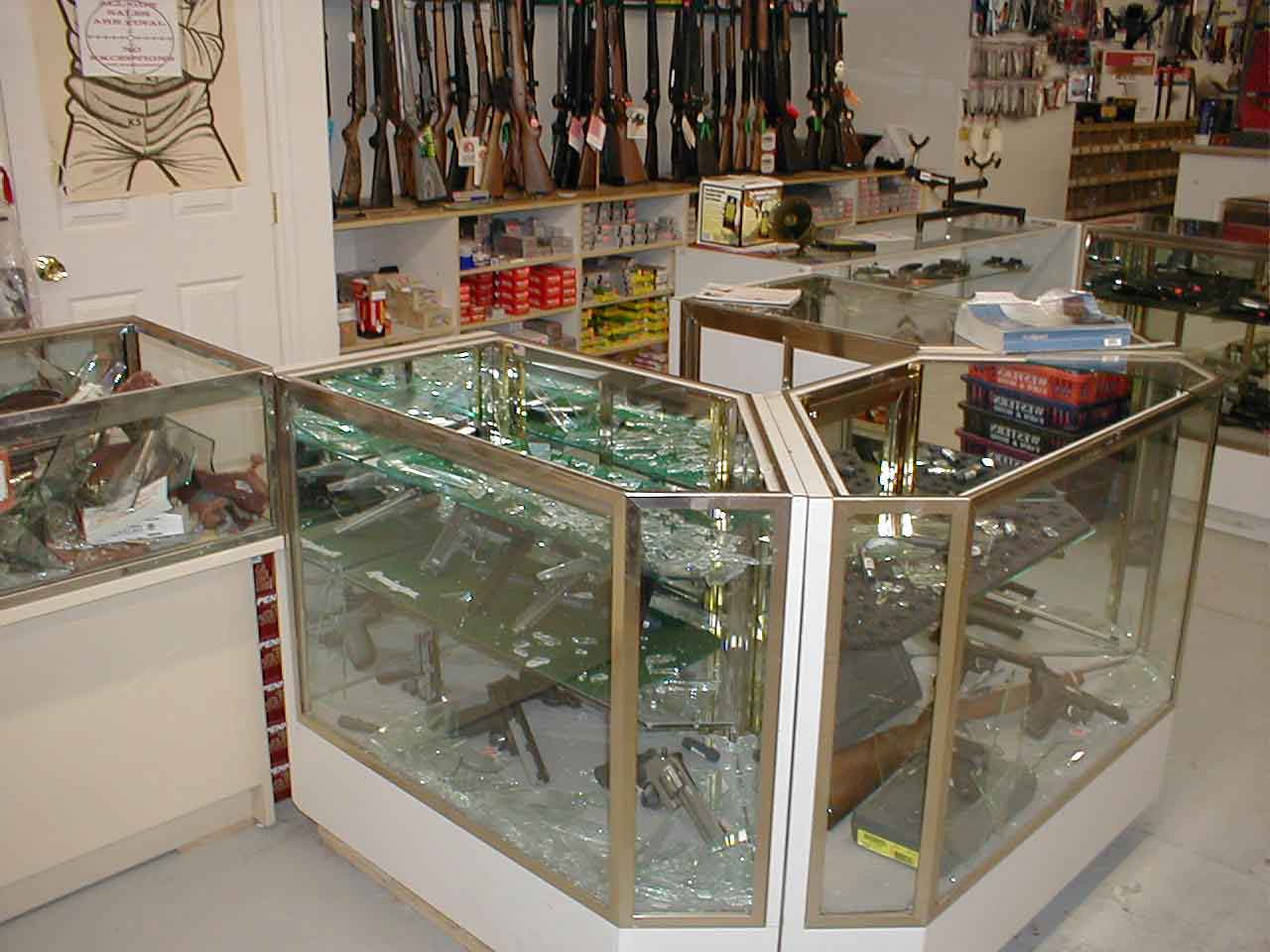 A different gun case that has been broken into. It is next to a register that sits in front of a long row of rifles for sale.