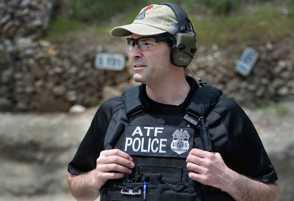 Michael Minichino at an outside gun range wearing a bullet-proof ATF Police vest