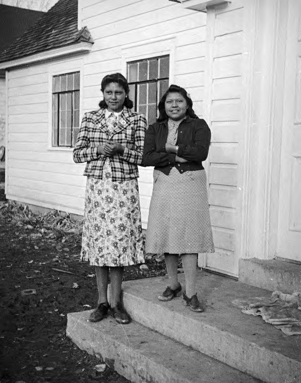 Two young women stand on a porch in this historic photo