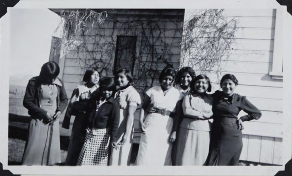 Historic image of girls dressed up smiling next to a house