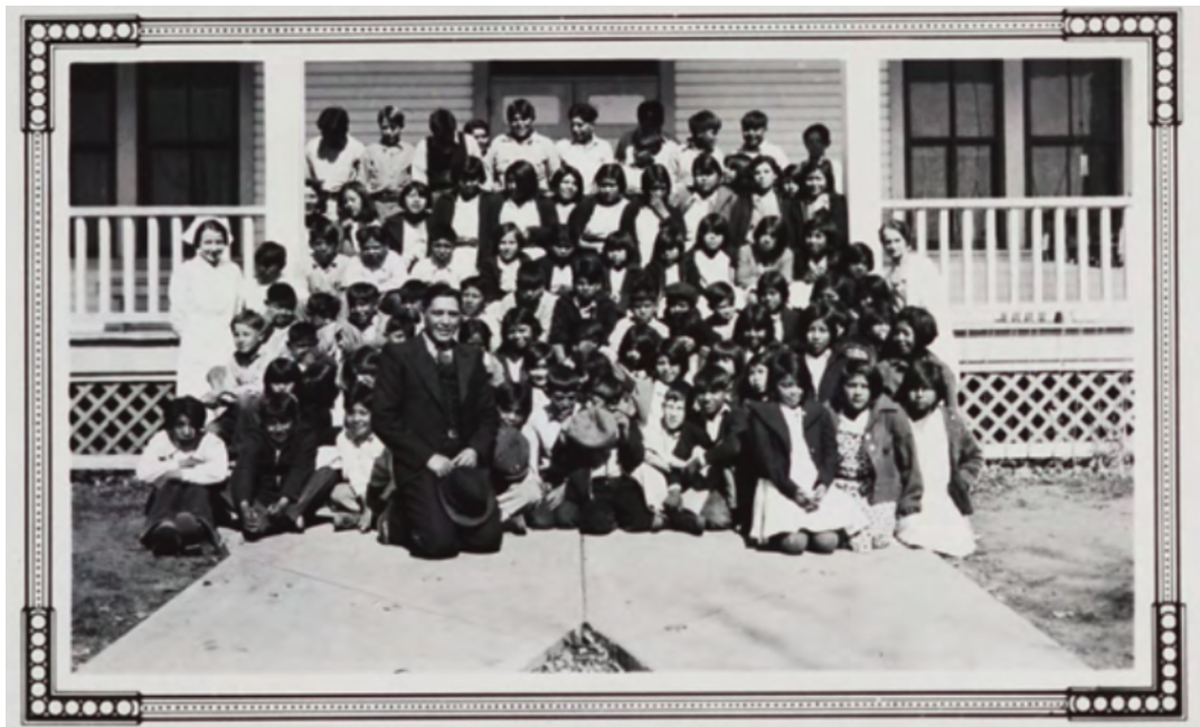 A large group of children sit in a porch for a group photo