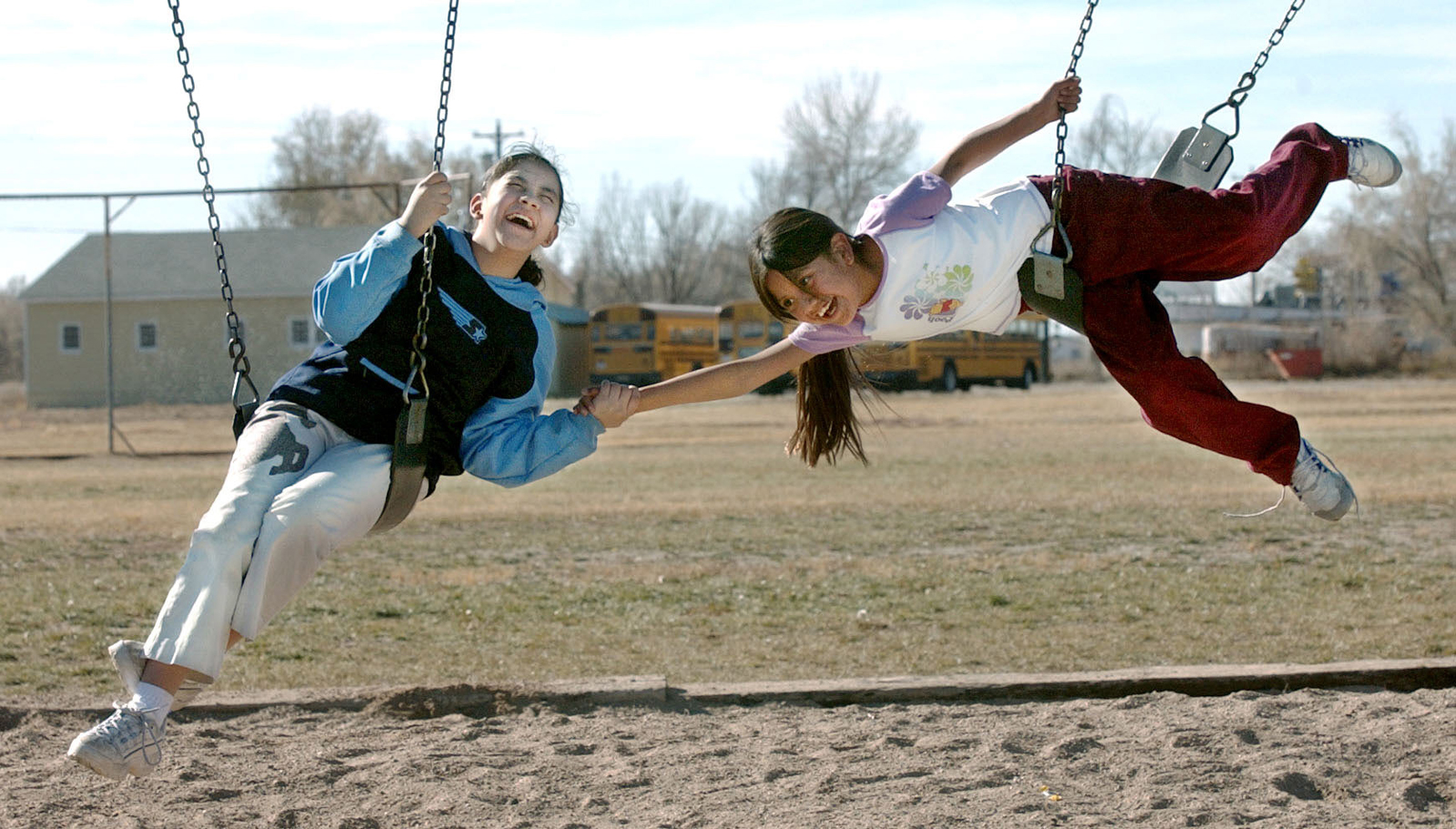 two school girls laugh on swings